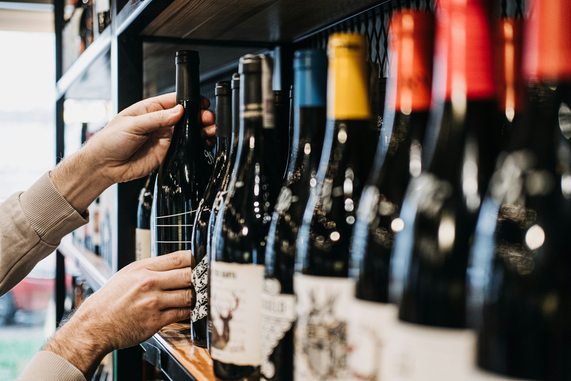 Customer Selecting Wine Bottle from Store Shelf. A person's hand picking a wine bottle from a